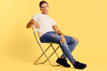 Cute man sitting on a chair white t-shirt jeans lifestyle modern style yellow background