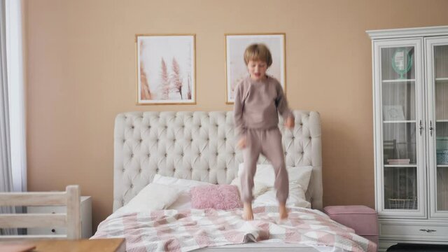 Caucasian boy jumping on bed having fun laughing playing funny active game with cute child son in bedroom