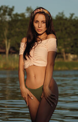 Obraz premium Sexy young brunette young woman standing in water at sunset