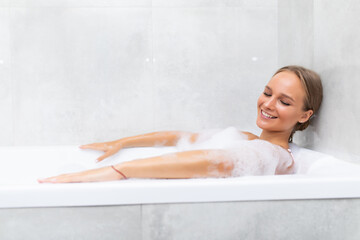 Happy young woman with foam lies in the bathroom and laughs