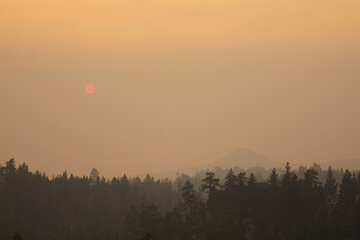 Very hazy and smokey view over Lake Tahoe near sunset, during wildfire season, with a red sun and trees in the foreground