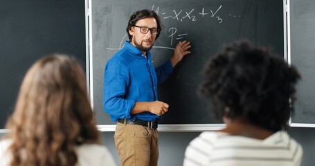 Caucasian man teacher at school writing formulas and mathematics laws on blackboard. School...