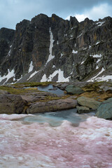 Fototapeta na wymiar étrange neige teintée de rose devant des montagne avec falaises à pic 