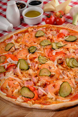 Pizza Bavaria. Rustic pizza with ham, tomato sauce, pepper, pickled cucumbers, onion, chicken meat, cheese on a wooden board for a dinner in italian restaurant background, top view. 