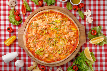 Rustic pizza with atlantic salmon, cheese, tomato, leek and tomatoes sauce on a wooden board for a dinner in italian restaurant background, top view. Classic Italy food. Close up