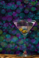 Glass of martini with olive on the background of bright lights in the bar