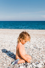 Fototapeta na wymiar Toddler girl playing with pebbles on beach