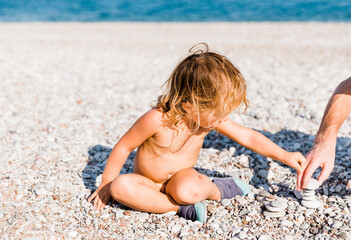 Toddler girl and man playing with pebbles on beach