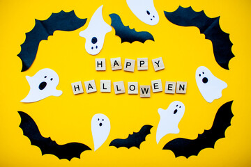 inscription from wooden blocks Happy Halloween and frame made of paper homemade bats and paper ghosts on a bright yellow background