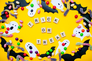 inscription from wooden blocks trick or treat and frame made of paper homemade bats and paper ghosts and multicolored candies and worms from gummy
