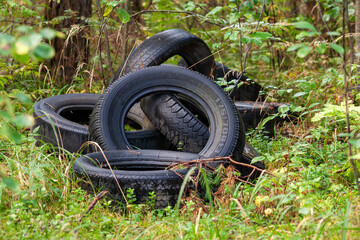 discarded car tires in the forest - illegal landfill, problem of nature pollution with consumer...