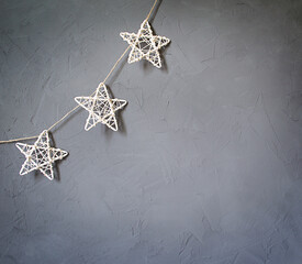 Christmas decorations in the form of stars hang on a gray concrete wall. Copy space.