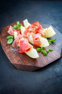 Modern Style traditionelle intalienische Antipasti mit Prosciutto di Parma und Honig Melonen Scheiben angeboten als close-up auf einem Design Holz Board 