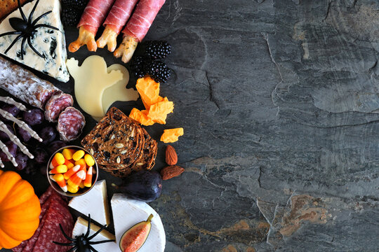 Halloween charcuterie side border against a dark stone background. Variety of cheese and meat appetizers. Copy space.