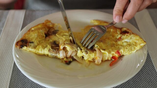 Closeup view 4k video of white plate and big fresh hot egg omelette stuffed with mushrooms, sweet red pepper, sausages and cheese. Woman eats healthy breakfast.