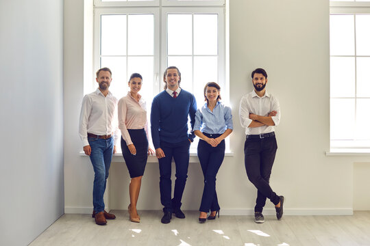 Group portrait of happy smiling company employees standing in modern office looking at camera