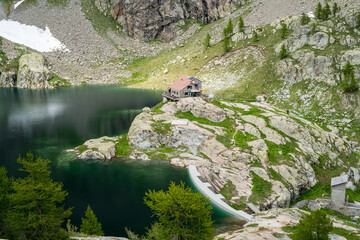 panorama sur un refuge de montagne au bord d'un lac vert 