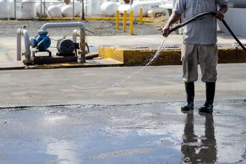 hombre mayor limpiando calle con una manguera, suelo mojado