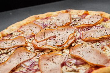 Delicious Italian Pizza with ham, onions and mozzarella cheese on dark background