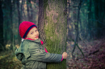 cute child hugging tree in autumnal forest