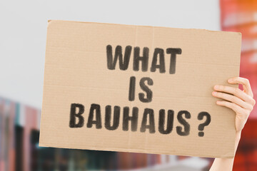 The question " What is Bauhaus? " on a banner in men's hand with blurred background. Architecture. Design school. Science. Engineering. Direction. Art movement