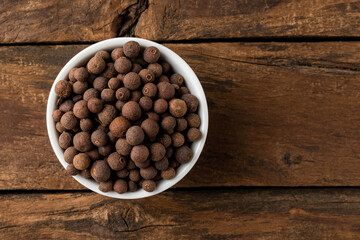 Allspice in bowl on rustic wooden table. Top view