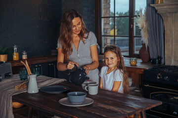 Happy loving family preparing dinner together. Smiling Mom and child daughter girl cooking and having fun in the kitchen. Homemade healthy food. Little helper in a dark kitchen interior at home