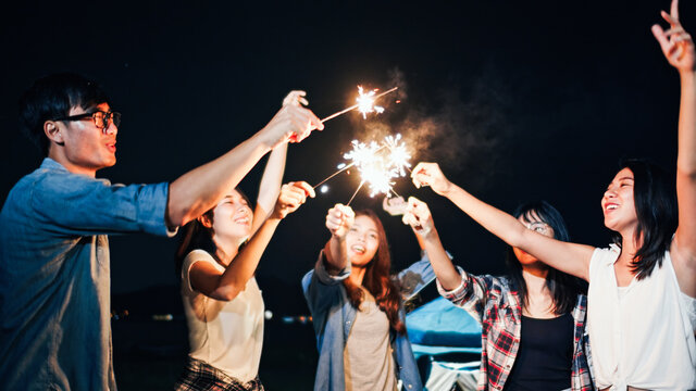 Group Of Young Asian College Student Friends Lit Light Sparkler, Sing And Dance Together At Beach Camping Tent. Party People, Love Friendship Relationship, Or Outdoor Camping Activity Concept