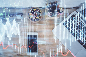 Double exposure of financial graph hologram over desktop with phone. Top view. Mobile trade platform concept.