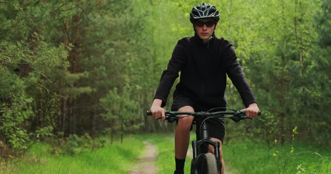 Young  man cyclist rides on a forest road. Teenager on a mountain bike rides through the forest. Man in a Bicycle helmet rides an mtb bike.