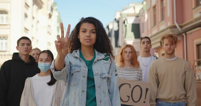 Mixed race woman leader at multiethnic protest shows peace gesture. Peaceful protesting demonstration.