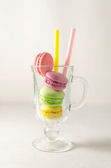 Multi-colored macaroons in a glass cup with straws for drinks on a linen napkin. Mcarons or macaroons is French or Italian dessert. Close-up.
