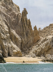 Cabo San Lucas, Mexico - April 22, 2008: Small beach on south end of Baha California surrounded by collection of beige rocks in greenish ocean water under light blue sky. 