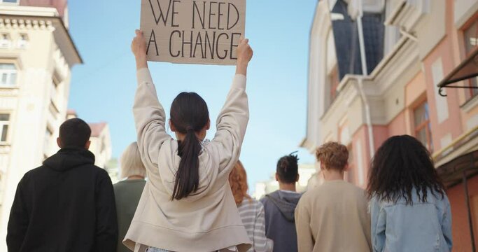 Asian woman in back of protest demonstration holding a poster We need a change. Student activist.