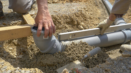 CLOSE UP: Plumbers use a level and fresh concrete to bury a wide sewage pipe.