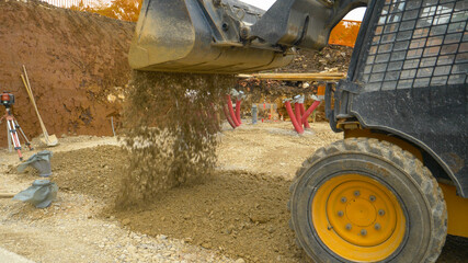 Fototapeta na wymiar CLOSE UP: Excavator unloads a big bucket full of wet gravel on leveled ground