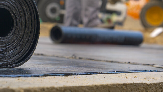 MACRO Detailed shot of a bitumen roll as worker burns a layer of hydroinsulation