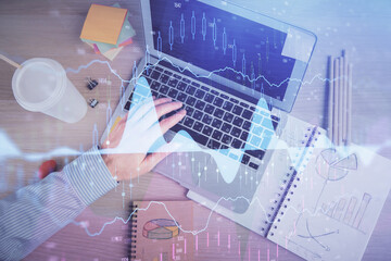 Double exposure of man's hands typing over computer keyboard and forex graph hologram drawing. Top view. Financial markets concept.