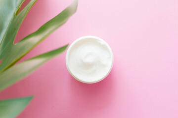 a jar of face cream, a body with green, exotic leaves next to it, on a pink background. Natural Care, Organic Cream, Moisturizing, Care, Beauty, Cosmetics Production