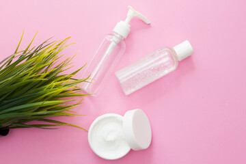 Set of cosmetic jars with organic cosmetics for face and body care on a pink background with green leaves. Cream, micellar water, shampoo and lotion on a light background. Layout, copy space.