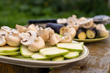 Delicious verious vegetables and champignon mashrooms in plates on wooden bench are prepared to be cooked on grille