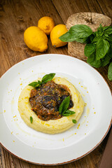 Veal cheeks are prepared by the chef, herbs and lemon zest on a plate. On a wooden table
