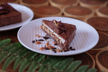 chocolate dessert in a cut with filling of caramel, nuts and nougats. The cake is covered with chocolate on a wooded background with a morning natural light
