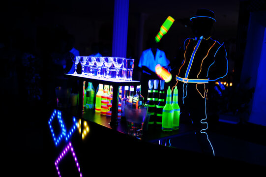 Professional barman and led light show. Silhouette of modern bartender shaking drink at night cocktail bar.