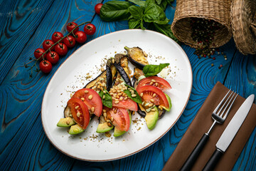 Salad with avocado, tomatoes, eggplant and pine nuts prepared by the chef on a plate. On a wooden table
