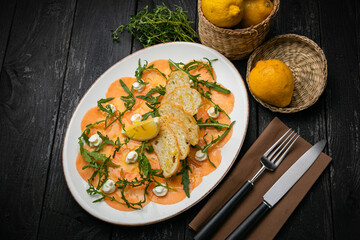 Salmon carpaccio on a plate with lemons, arugula, goat cheese and croutons

