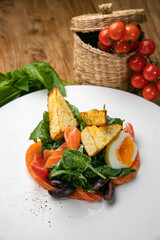 Salmon salad on a plate with egg, herbs, spinach and croutons. On a wooden table
