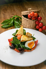 Salmon salad on a plate with egg, herbs, spinach and croutons. On a wooden table
