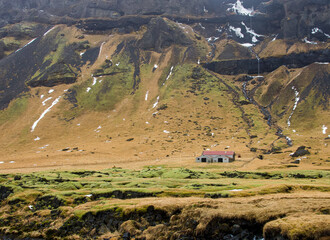 Barn surrounded by orange and green mountains with a waterfall and snow