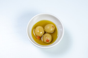 Green olives in a small casserole with olive oil on a white surface background
